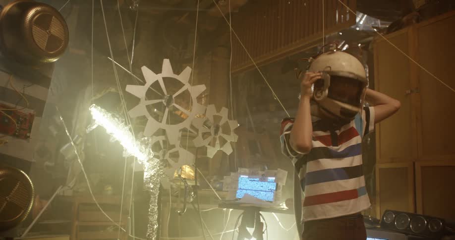 Young boy playing inside a shack puts on an astronaut helmet