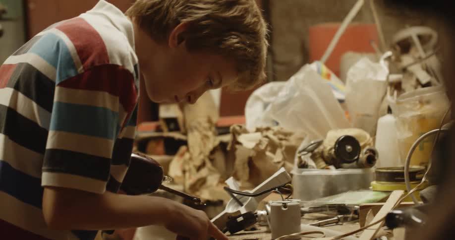 A boy in a workshop holding a soldering iron and some solder