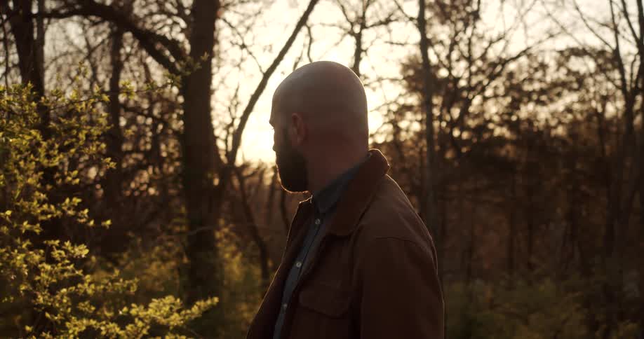 Sun shines through trees briefly turning man standing in woods into a silhouette