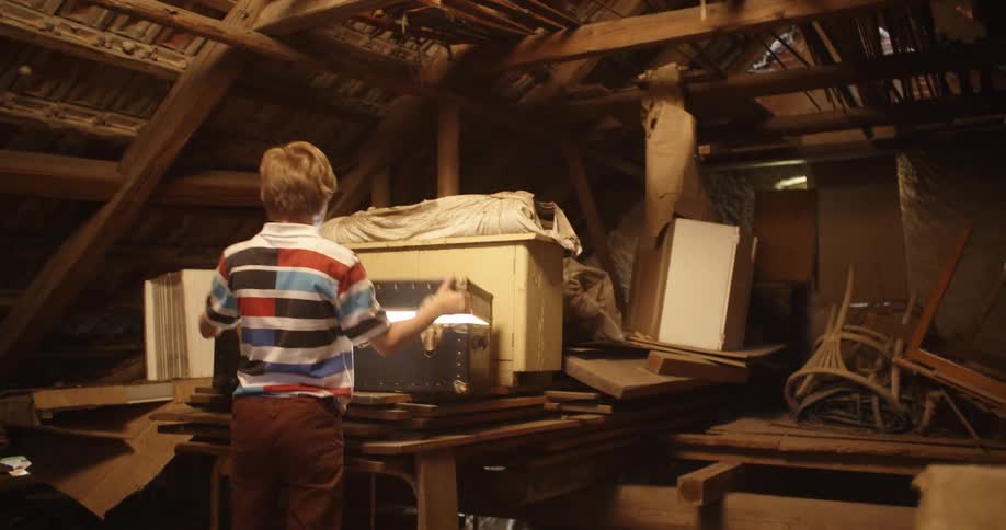Young boy playing in the attic finds and opens a chest with a bright light inside