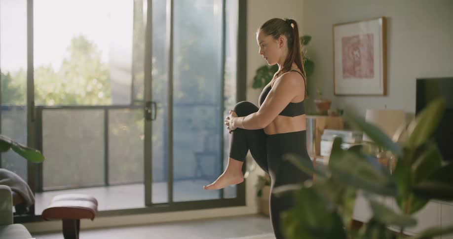 Woman stretches balancing on one foot while exercising in living room