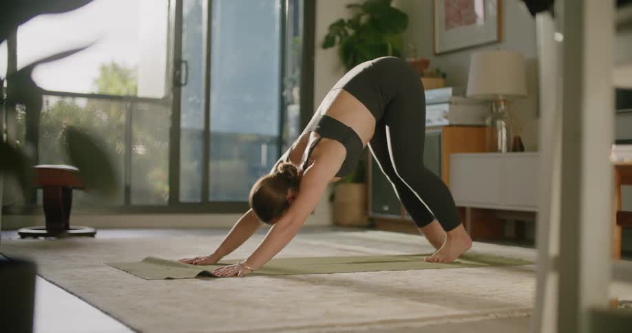 Young woman wearing sports clothes stretches over a mat in the living room