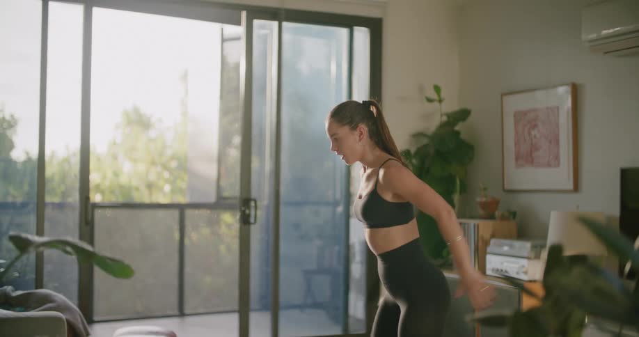 A woman in a room exercising with a wall and a plant in the background