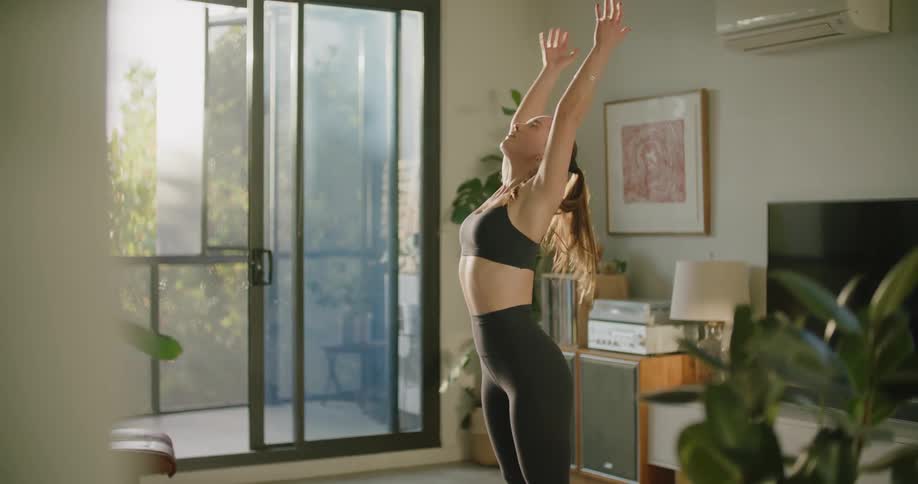 Young woman wearing sports clothes stretches over a mat in the living room