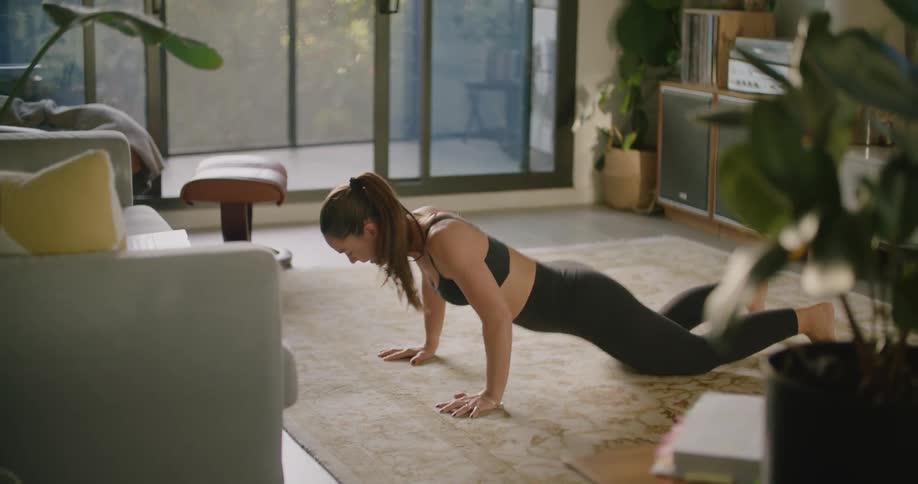 A woman does push up burpees while working out in the living room in her condo