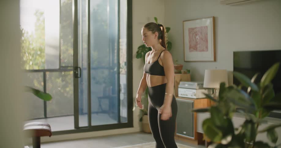 A young woman stands indoors and stretches her arms above her head as she prepares to exercise