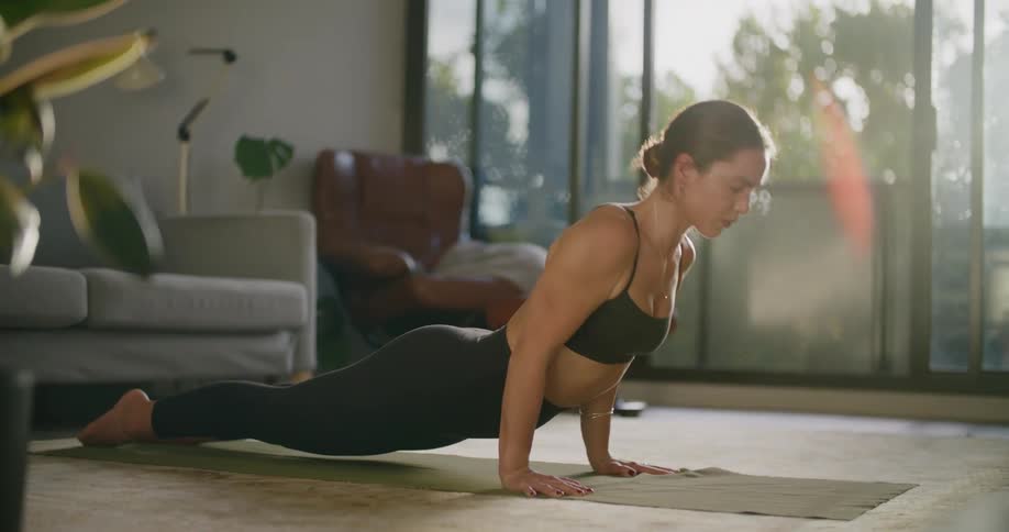 A woman in a room working out and stretching with a couch and a wall in the background