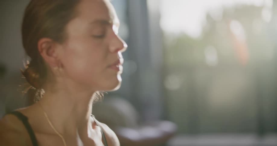 Woman straightens up meditating with closed eyes in sunny area
