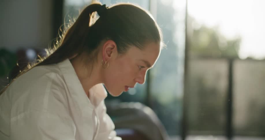 A female taps her finger on a table and looks deep in thought before typing on the laptop in front of her
