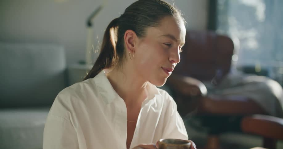 A woman in a room holding a smoking mug with a couch and a wall in the background