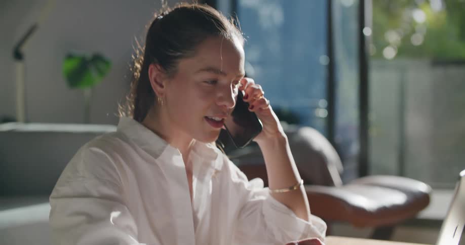 A woman working on a laptop while talking on a phone