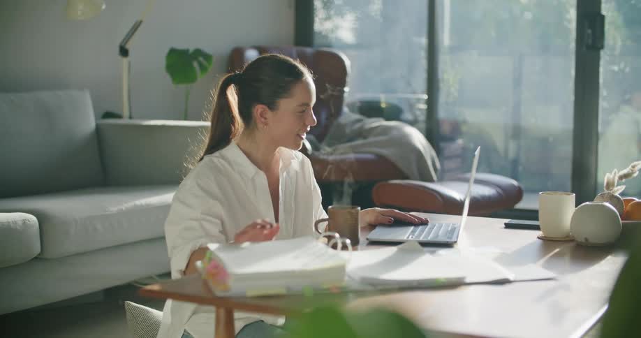 A woman sitting by a table using a laptop next to a mug with a couch in the background
