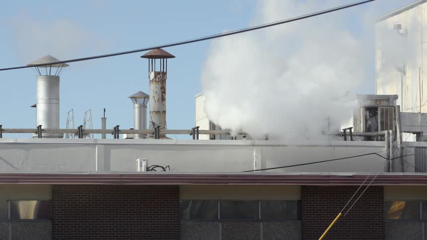 White vapor is exhausted from roof of building under blue sky