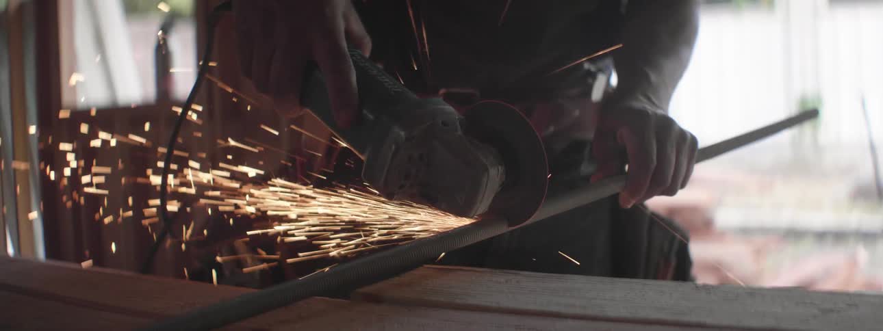 A man uses a circular saw to cut a piece of rebar during the day