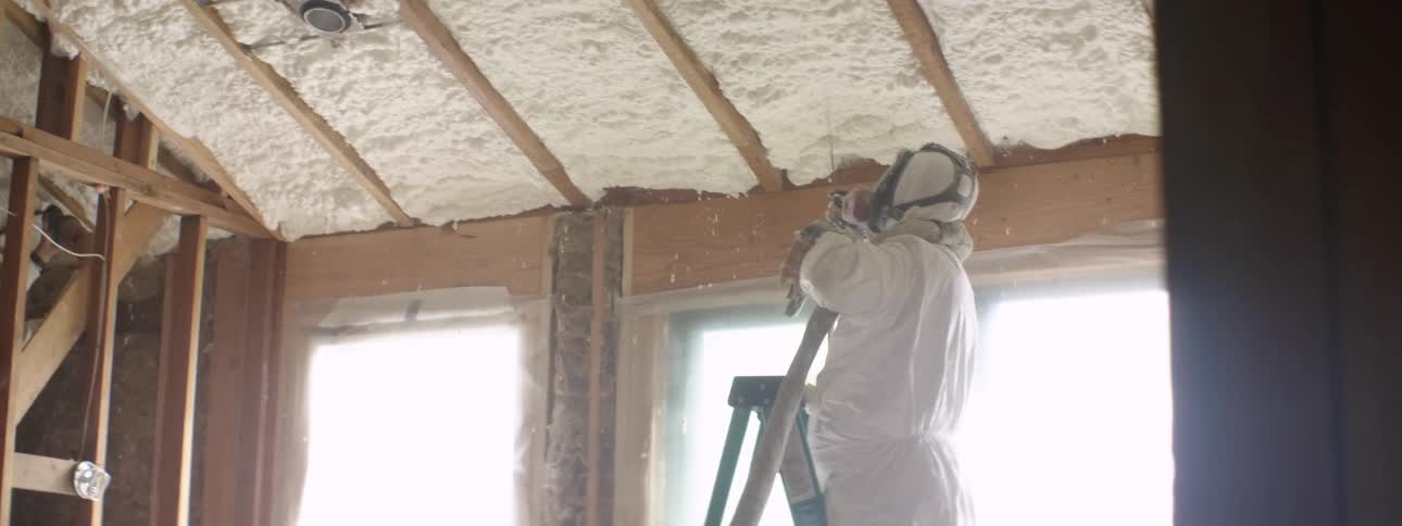 A worker in a face mask installing insulation in a ceiling