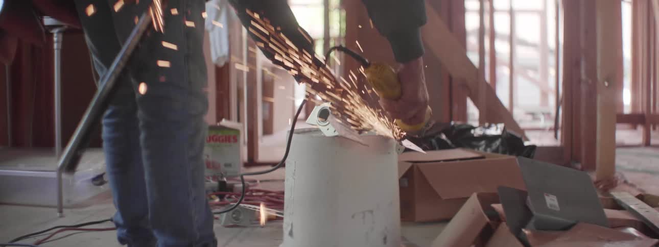 A construction worker uses a bucket as a saw horse to cut metal and sparks fly