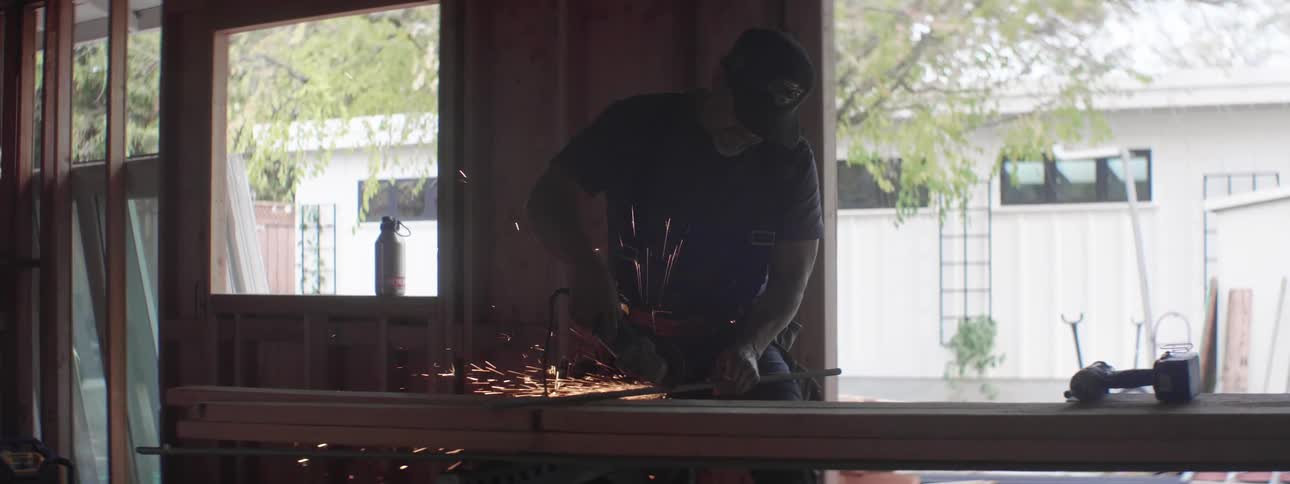 A man with a hat using an electric saw to cut a metal rod with sparks