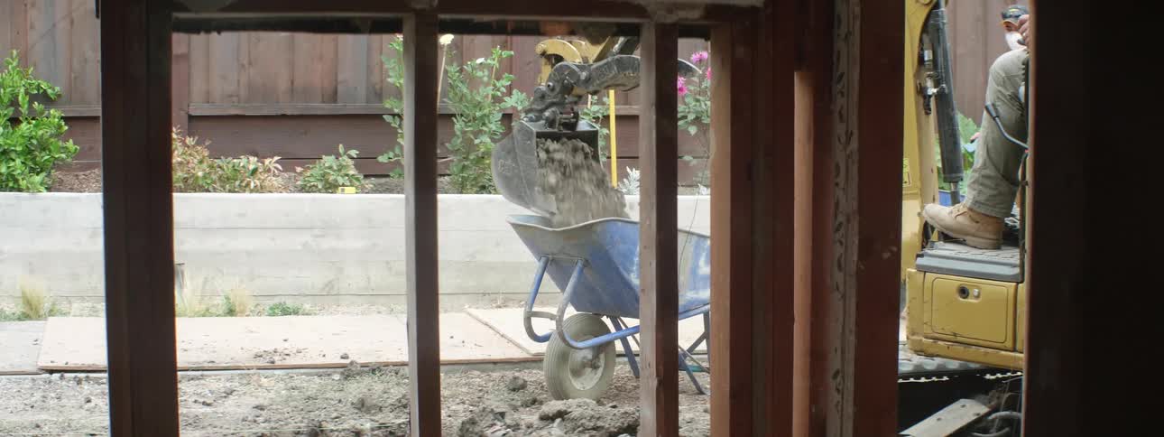 An excavator in a construction site moves dirt from the ground into wheelbarrows