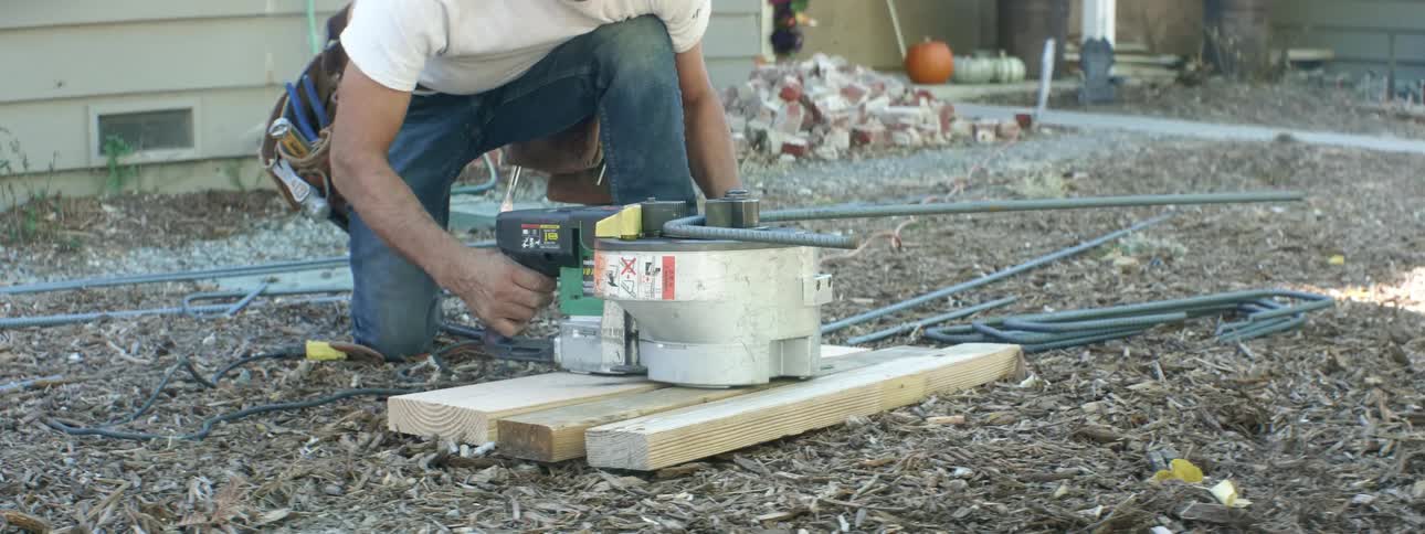 Kneeling on ground near house man uses machine to shape metal bars