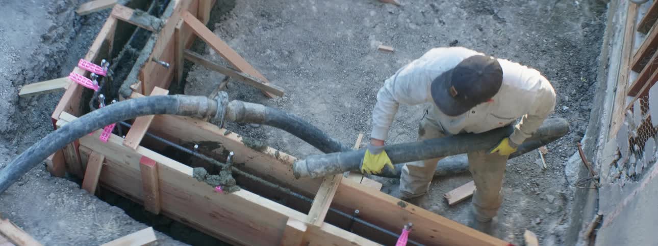 A man with a hat and gloves pouring cement from a hose