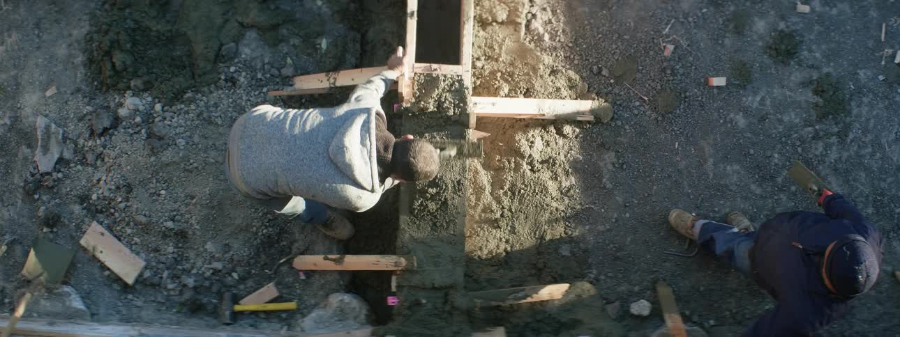 An aerial view of a man watching another man smooth cement in a wood frame