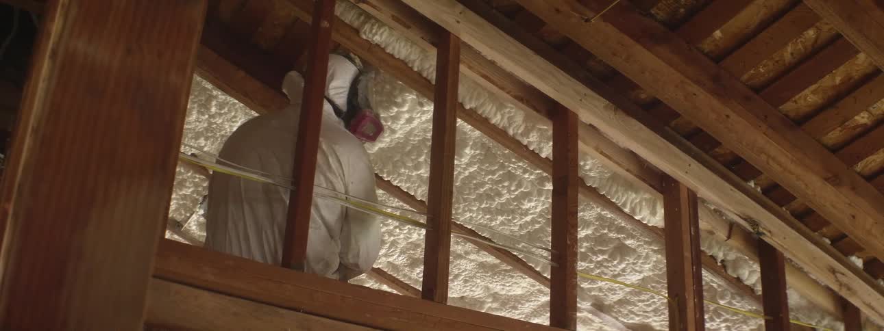 A person in a hazmat suit is spraying insulation in a home