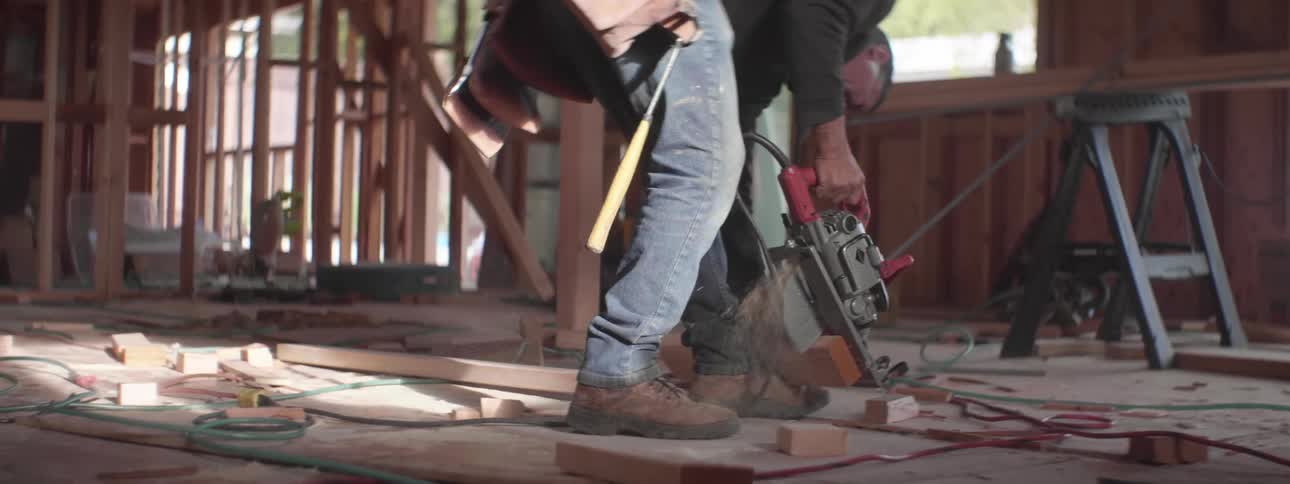 A man uses a circular saw to quickly cut a block of wood in a building under construction during the day