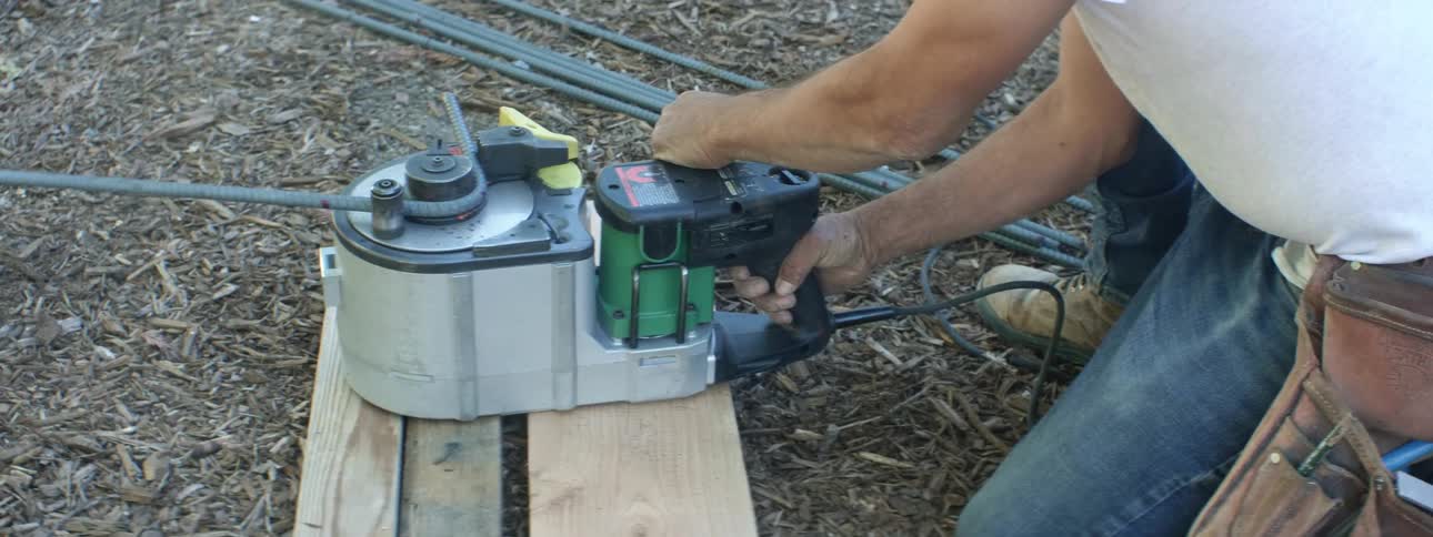 A person with boots and a utility belt using a machine to bend metal