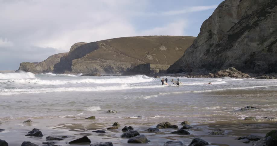 People with surfboards walking on a beach with a cliff the sky and clouds in the background