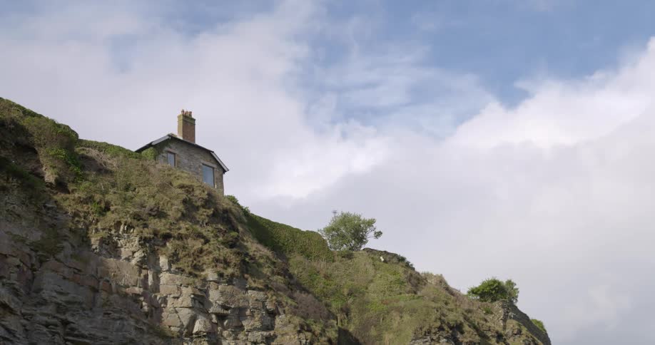 A small cobblestone house near the edge of a cliff in the mountains