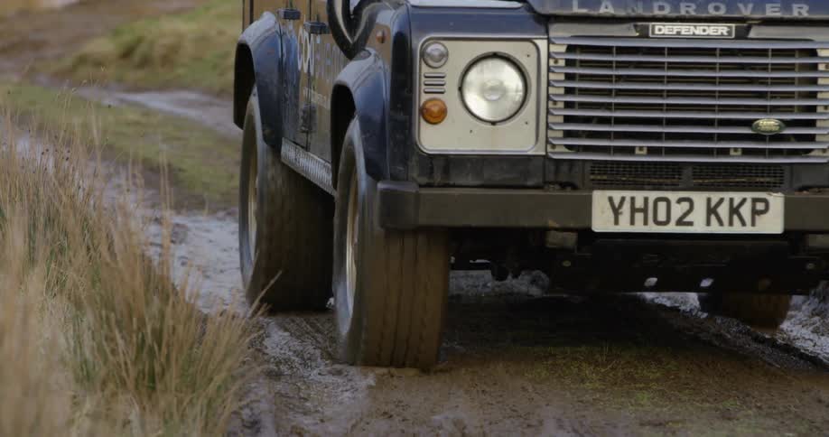 A land rover travels on a muddy dirt road
