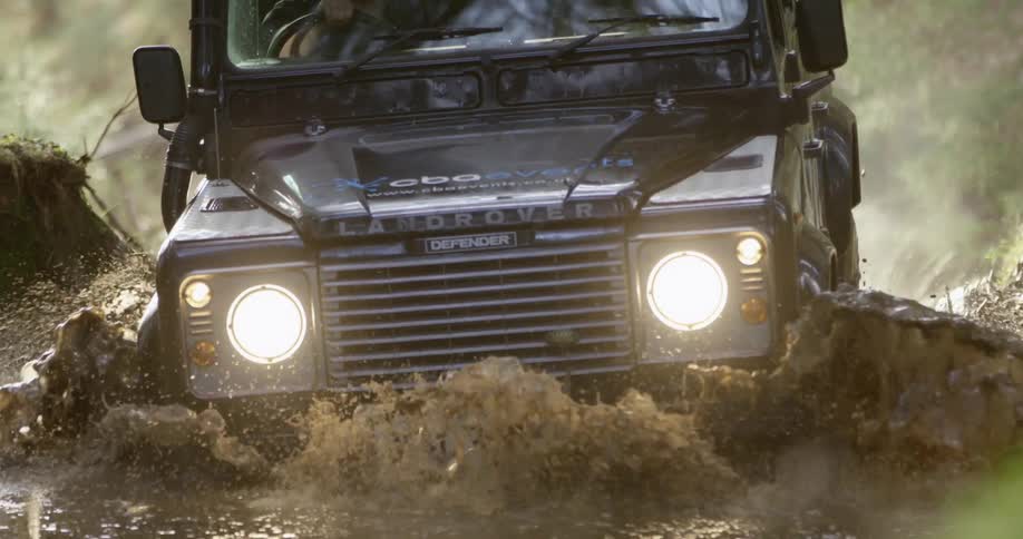 A landrover sport utility vehicle drives through a large puddle while offroading