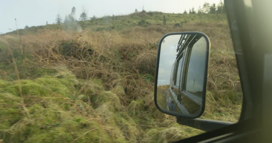Side mirror reflects side of vehicle traveling passed hill