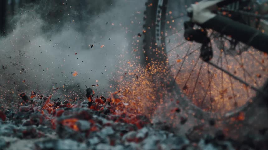 Burning ashes and embers fly into the air as bike tires roll over them among the flames of a forest fire