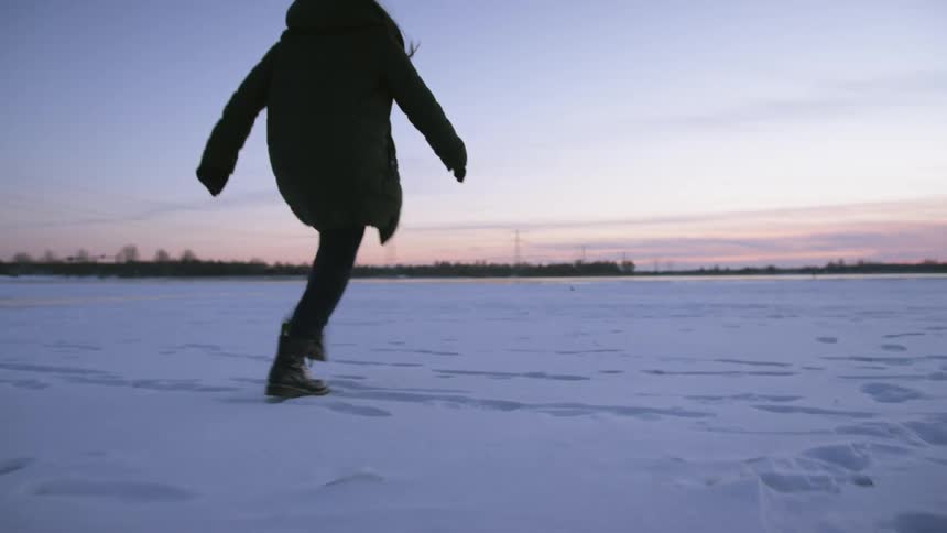 A woman leaves footprints in the snow from her combat boots as she runs through a flat field
