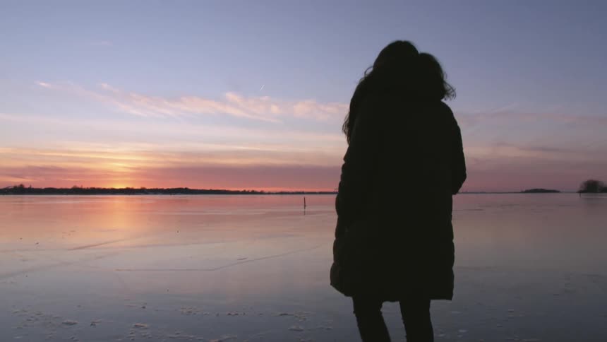 A woman is walking on the beach at sunset