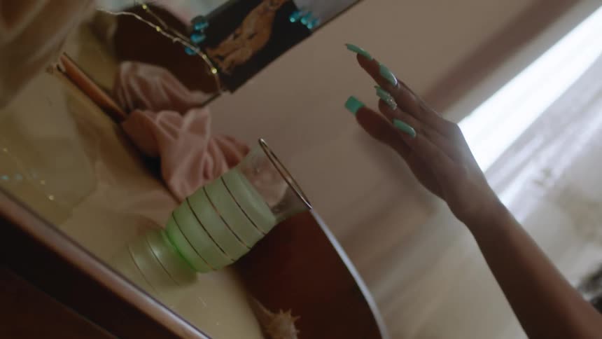 A woman places her manicured hand over a dresser and causes a glass of water to shake