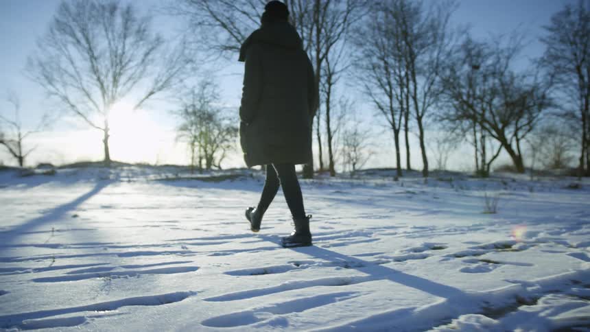 Woman wearing a coat walking on the snow near a treeline at sunset