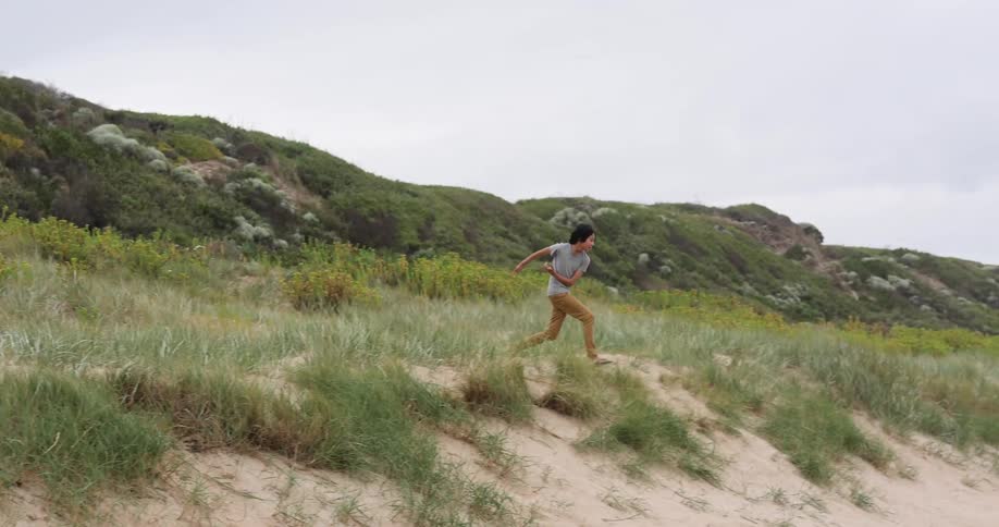 Young boy running and jumping over a sand dune near the beach