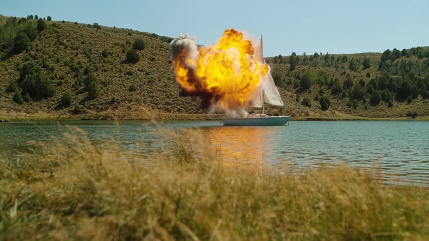 Flame and smoke flow from sailboat floating in narrow waterway near hill