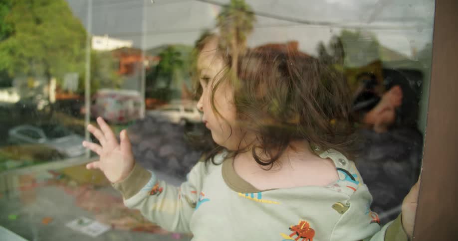 Baby girl looking out the window of the bedroom at home
