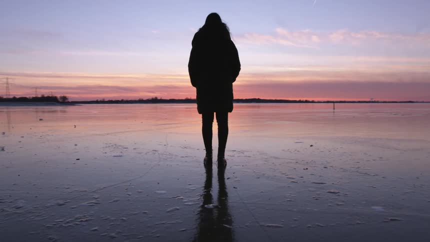 A woman is standing outdoors as the sun is setting