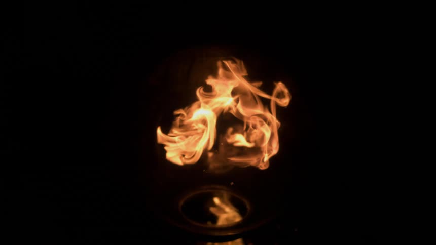 Fire bursts upward in the darkness and the flames are contained inside a clear globe