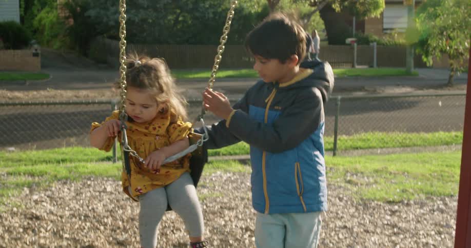 A young boy pushes his little sister in a swing