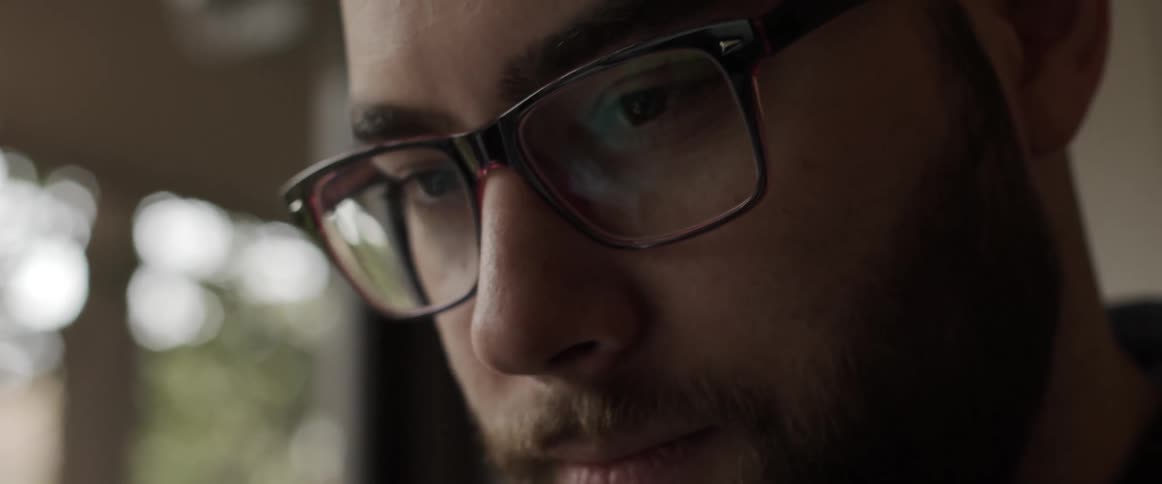 A man in a room with glasses with a wall and window in the background