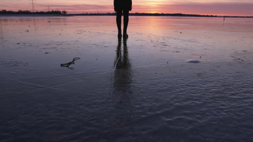 A silhouette person standing alone on a wet sandy beach at sunset