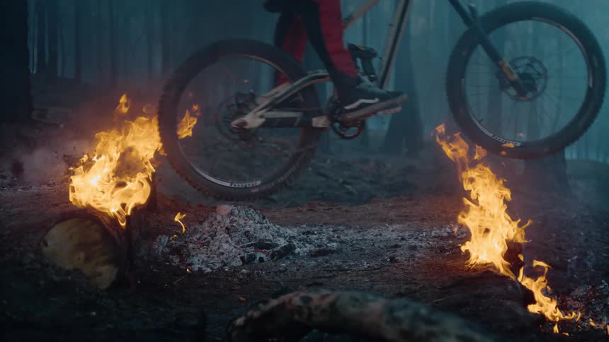 Person on bicycle rides down flaming logs in smokey woods