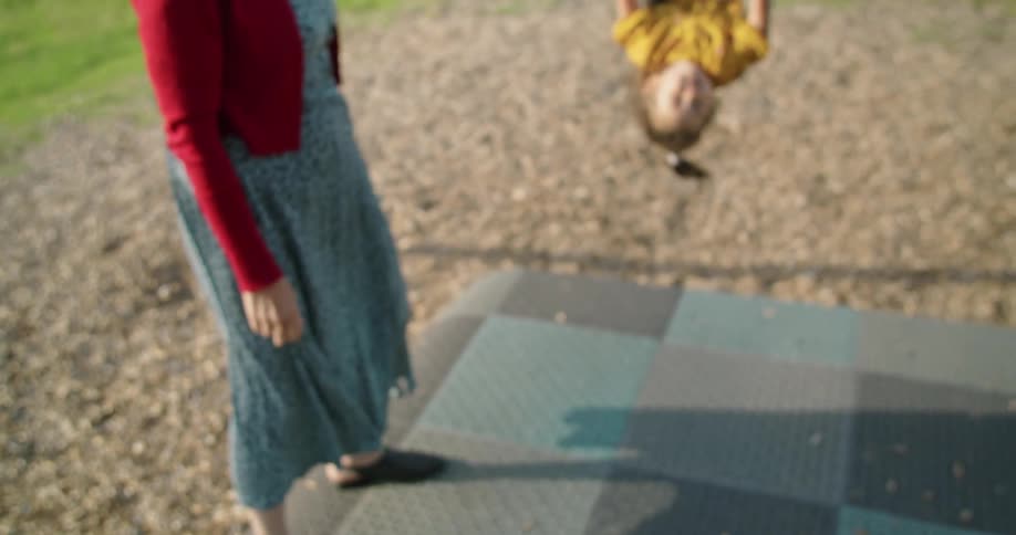 Girl swings in playground as woman stands and watches