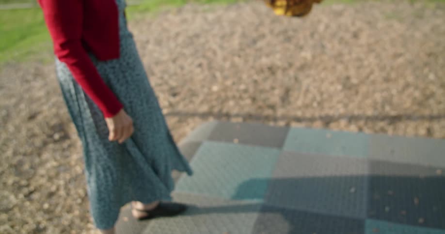 A girl swinging on a swing next to a woman in a dress with gravel and grass in the background