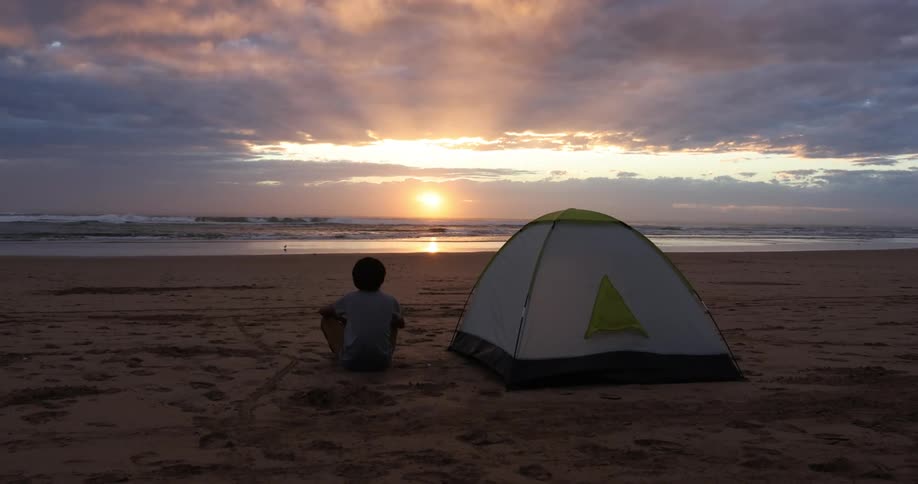 A person is sitting at the beach at dusk